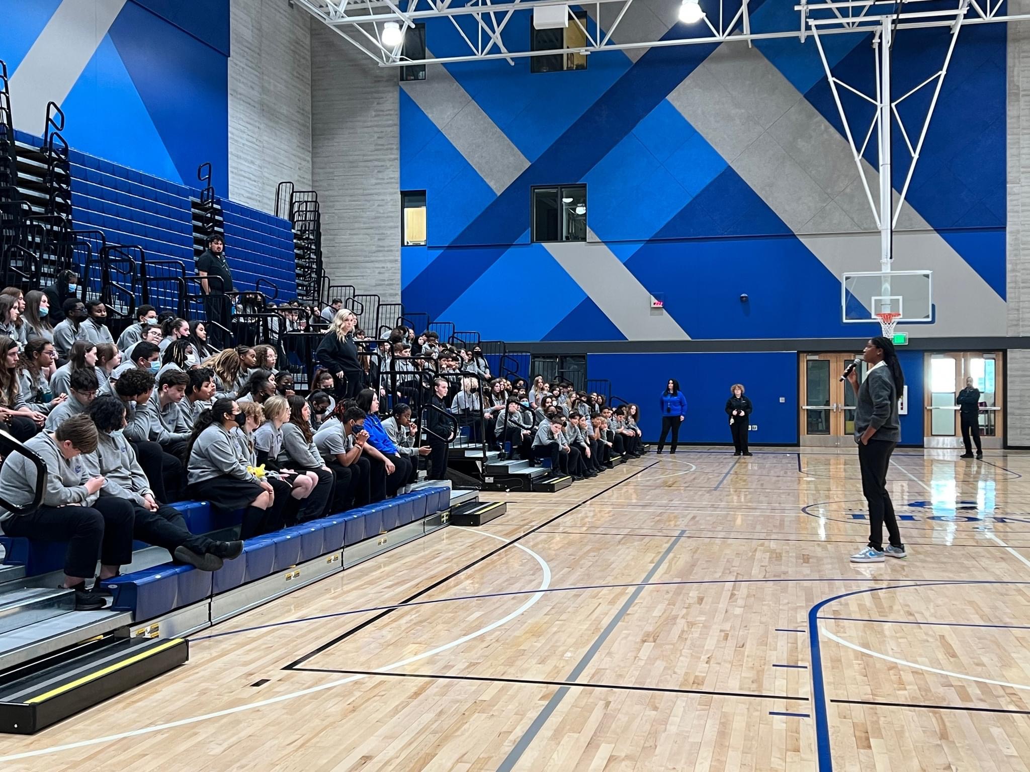 Michelle Snow addressing students seated in the bleachers of a school gymnasium