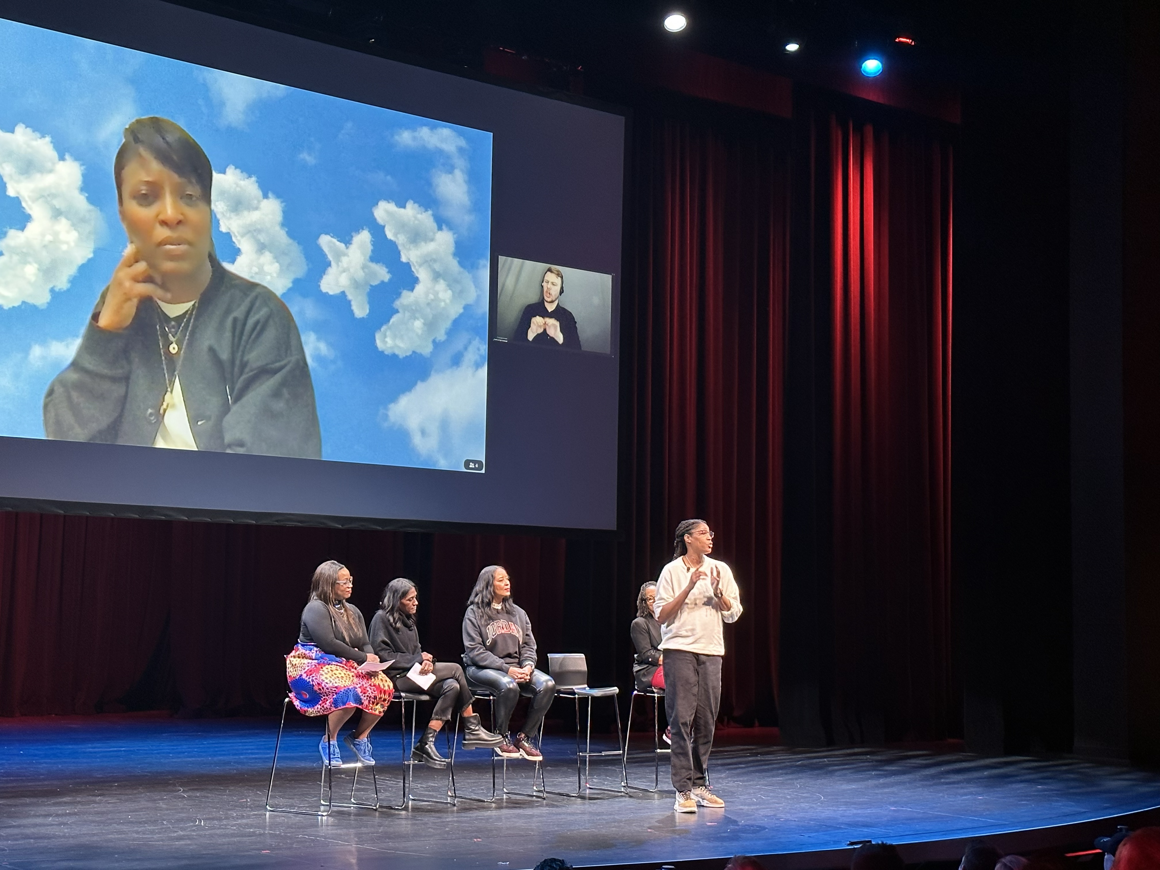 Michelle Snow on a theater stage panel with a virtual speaker projected on the screen