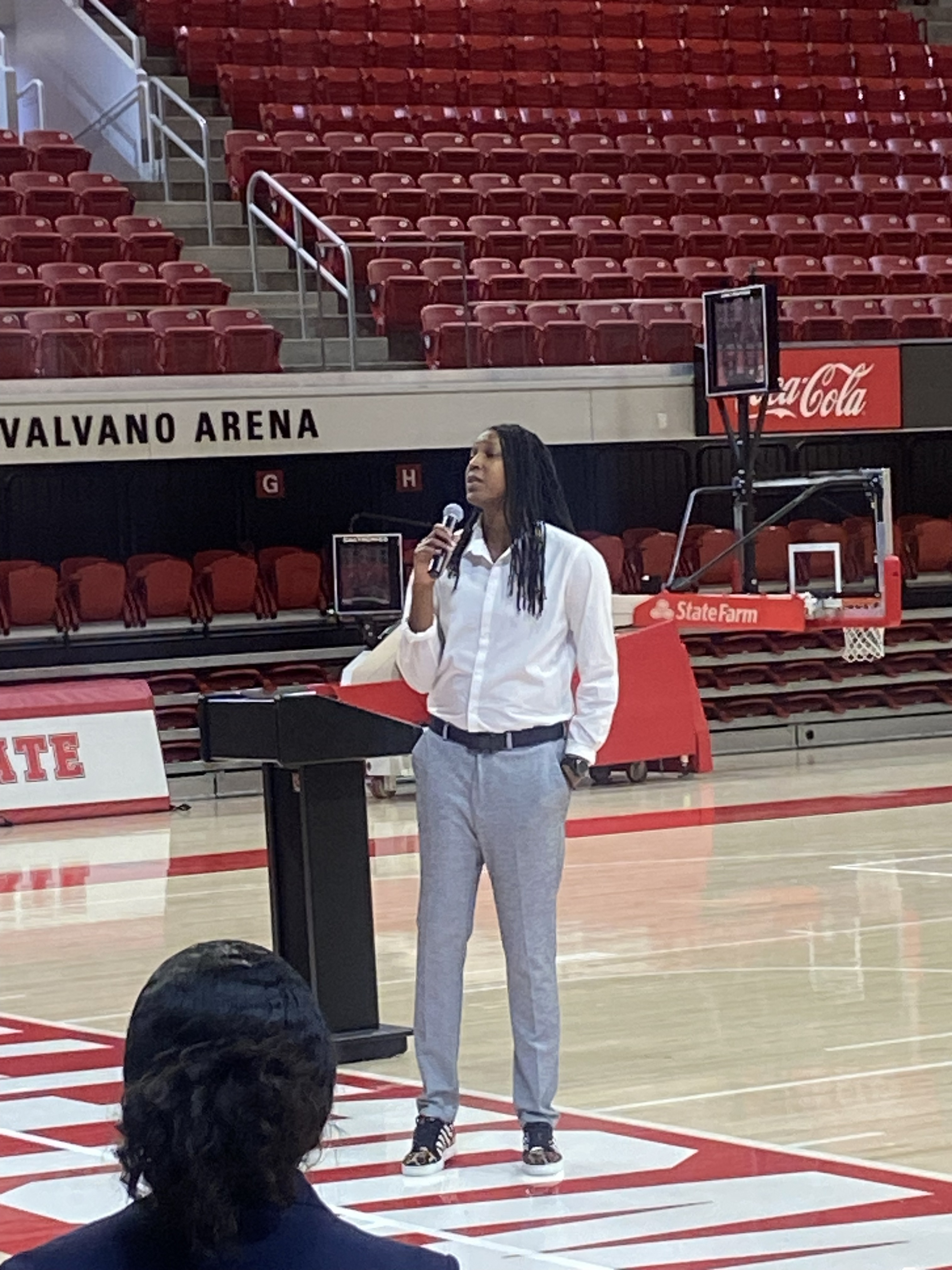 Michelle Snow speaking with a microphone on the court at Reynolds Coliseum's Valvano Arena